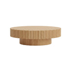 Round wooden coffee table in a living room setting with decor items.