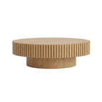 Round wooden coffee table in a living room setting with decor items.